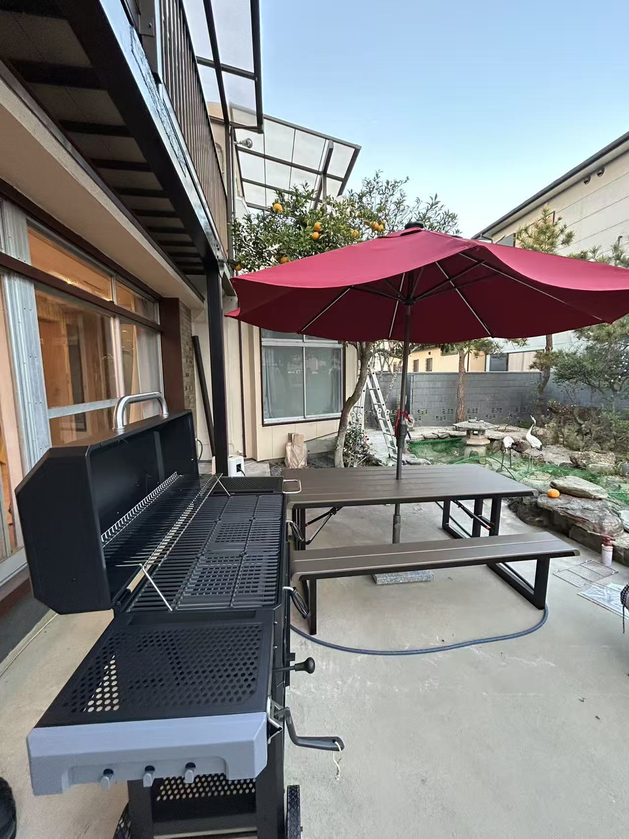 蓋を開けた大型BBQグリルと庭